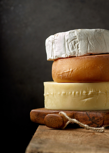 Drei Käsesorten sind übereinander gestapelt auf einem Holzbrett.