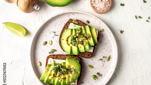Zwei Brotscheiben mit Avocado und Microgreens auf einem Teller, daneben Limetten, Salz und Pfeffer.