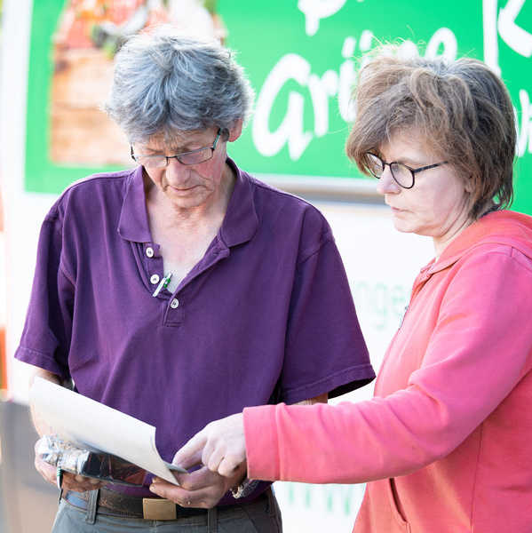 KI generiert: Zwei Personen betrachten gemeinsam ein Dokument vor einem grünen Schild. Textdetails sind nicht vollständig lesbar.