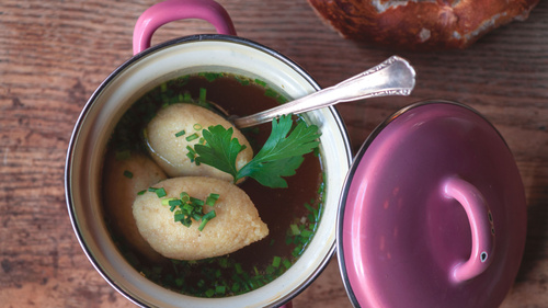Ein rosafarbener Topf mit Grießklößchensuppe, garniert mit Petersilie.