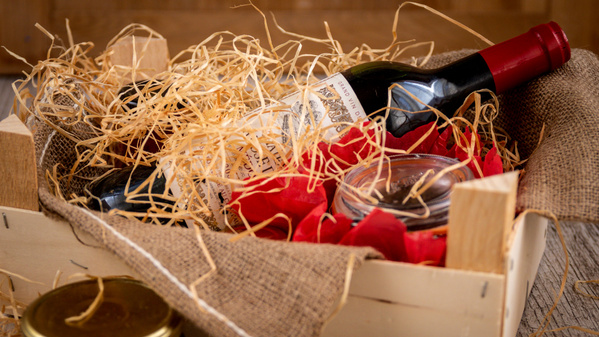 Holzkiste mit Weinflasche, Heu und Geschenkverpackung.