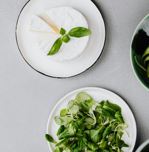 Teller mit Camembert, Basilikum, frischem Salat, Limette und Birne auf grauem Hintergrund.