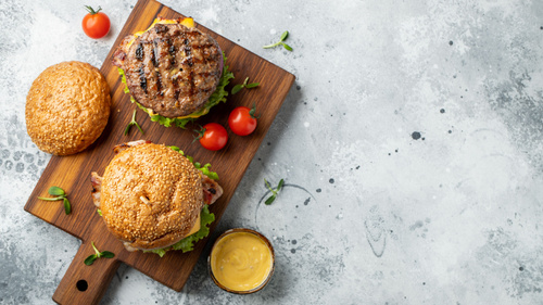 Burger auf Holzbrett mit Kirschtomaten und Senfsoße.