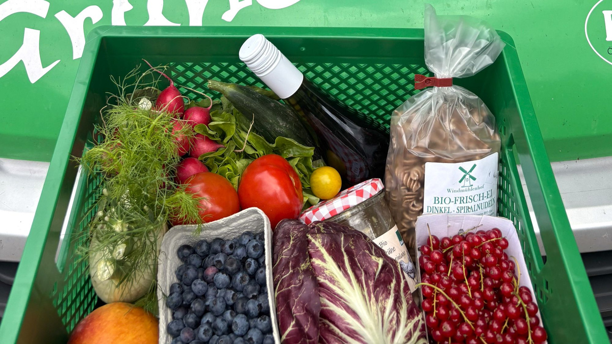 KI generiert: Gemüsekiste mit verschiedenen Obst- und Gemüsesorten, Nudeln und einer Flasche Wein. Text: "BIO-FRISCH-EI DINKEL-SPIRNUDELN".