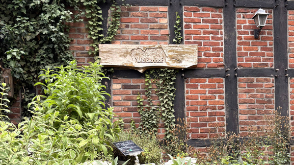 Ein Schild mit dem Namen "Weidenhof" an einer Backsteinmauer.