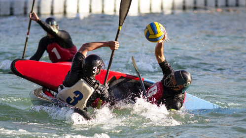 Drei Kanupolospieler kämpfen um den Ball im Wasser.