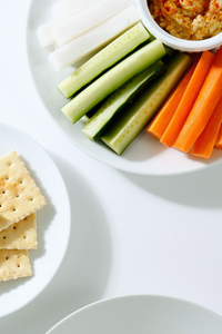 Gemüse-Sticks mit Dip und Cracker auf weißen Tellern.