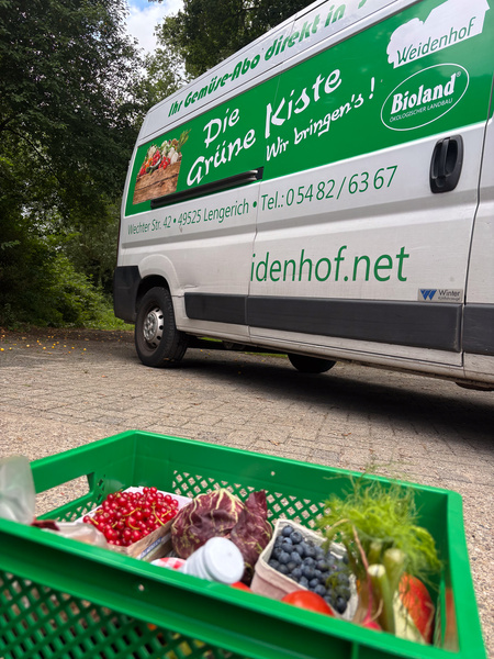 KI generiert: Ein Lieferwagen von "Die Grüne Kiste" und eine Gemüsekiste mit frischen Produkten. Text: "idenhof.net".