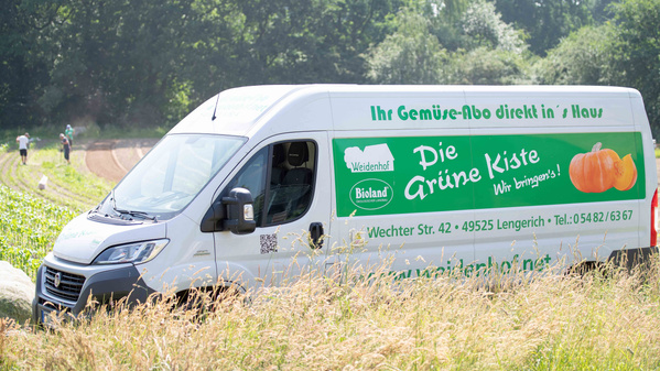KI generiert: Ein Lieferwagen mit Werbung für "Die Grüne Kiste" und Service-Details im Vordergrund.