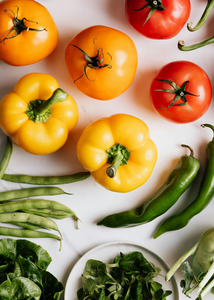 Verschiedenes frisches Gemüse wie Tomaten, Paprika und Bohnen auf einer weißen Oberfläche.