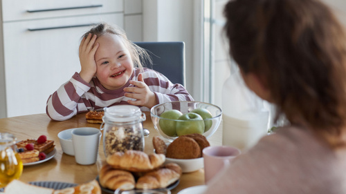 Ein Mädchen lacht beim Frühstück mit Croissants und Obst auf dem Tisch.