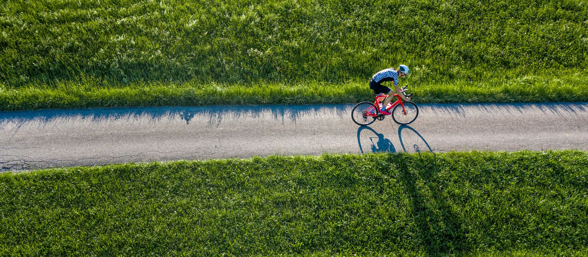 KI generiert: Eine Person fährt auf einem roten Fahrrad einen schmalen Weg entlang, umgeben von grünen Feldern.