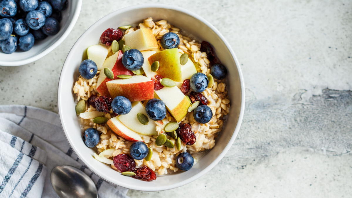 Eine Schale Müsli mit Apfel, Heidelbeeren, Nüssen und Kernen auf einem Tisch.