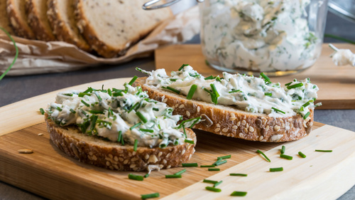 Brotscheiben mit Frischkäse und Schnittlauch auf einem Holzbrett.
