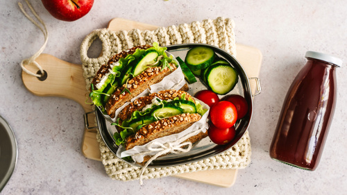 Lunchbox mit belegten Broten, Gurken, Tomaten und einem roten Getränk.