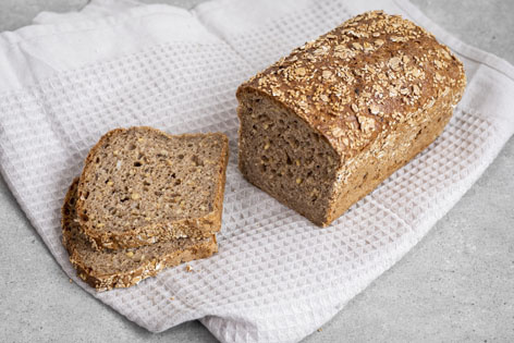 KI generiert: Ein Laib Vollkornbrot mit zwei abgeschnittenen Scheiben auf einem weißen Tuch.