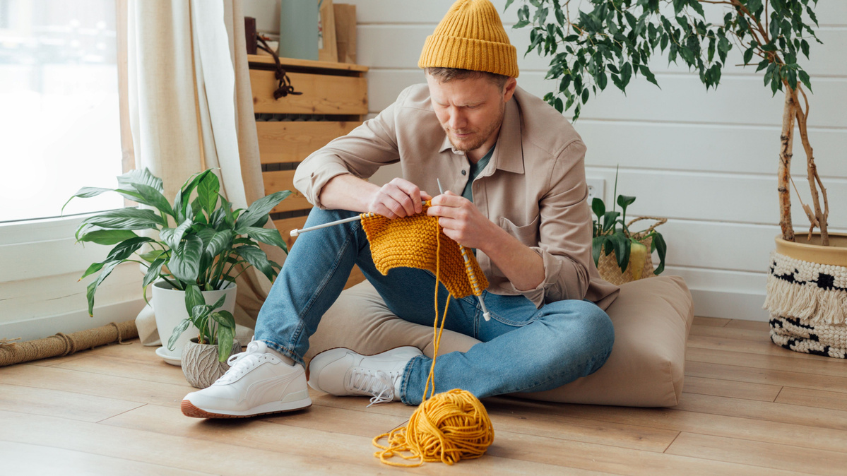 Ein Mann strickt mit gelber Wolle