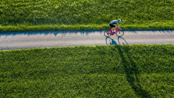 Radfahrer auf einem Feldweg, flankiert von grünem Gras, aus der Vogelperspektive. by Adobe Stock, Stefan Schurr