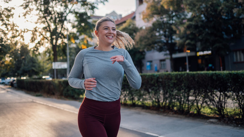 Frau joggt lächelnd in urbaner Umgebung bei Sonnenuntergang.