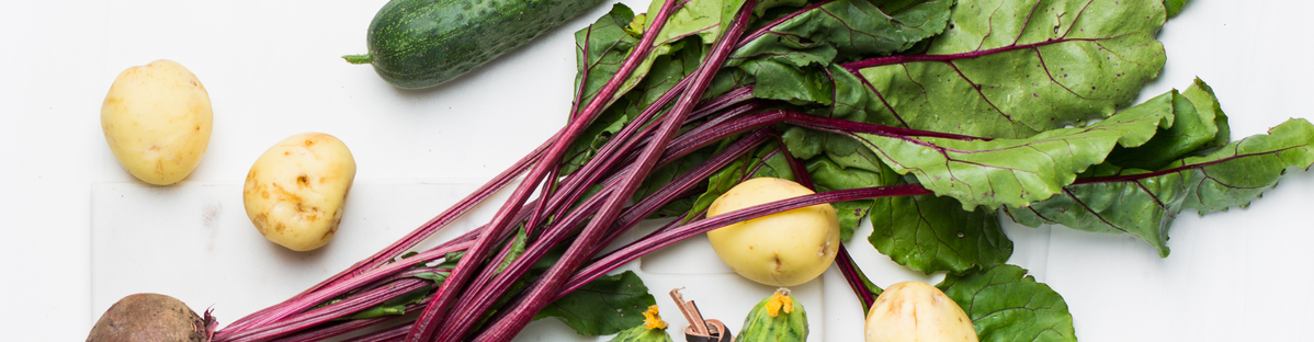 KI generiert: Verschiedenes Gemüse, darunter Kartoffeln, Gurke und Rote-Bete-Blätter, liegt auf einer weißen Oberfläche.