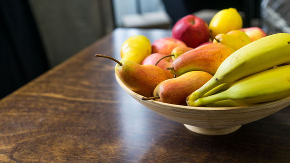 KI generiert: Eine Schale mit verschiedenen Früchten, darunter Bananen, Birnen und Äpfel, steht auf einem Holztisch.