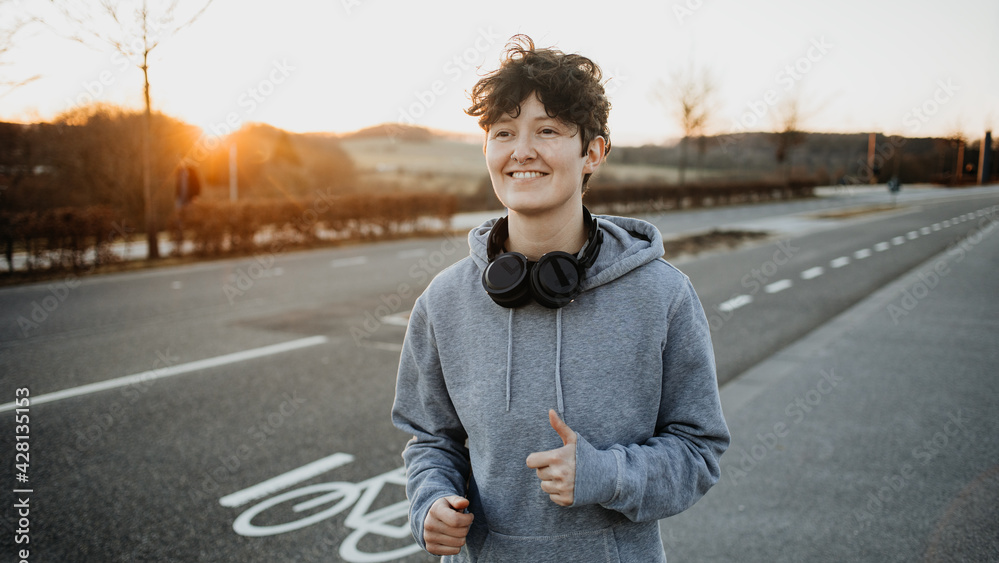 KI generiert: Eine Person joggt auf einer Straße bei Sonnenuntergang und trägt Kopfhörer um den Hals.